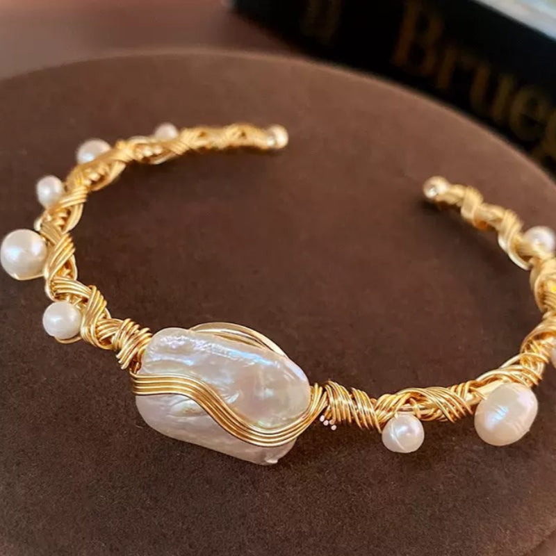 Gold wire-wrapped bracelet with a large, iridescent baroque pearl and smaller pearls.