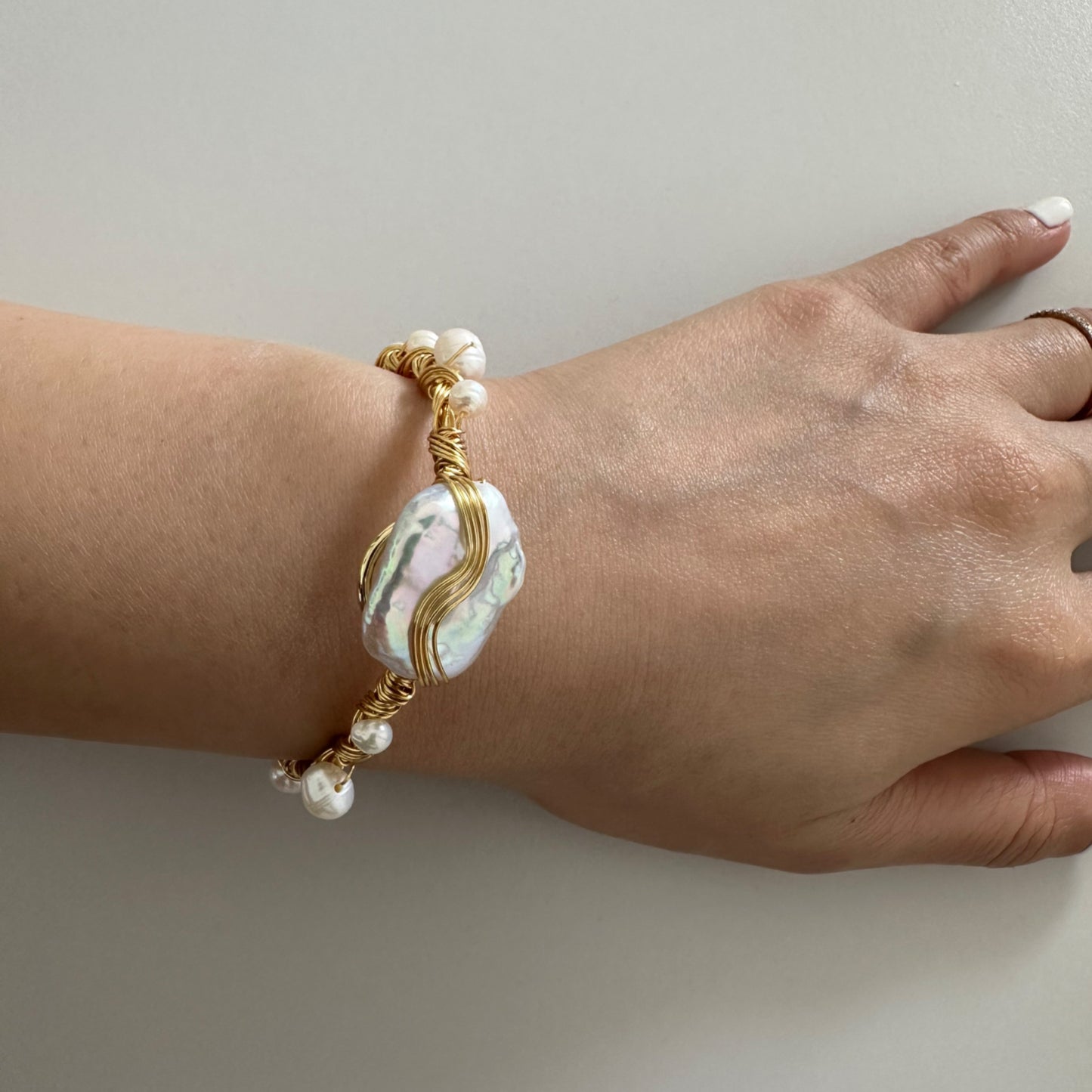 Gold wire-wrapped bracelet with a large, iridescent baroque pearl and smaller pearls.