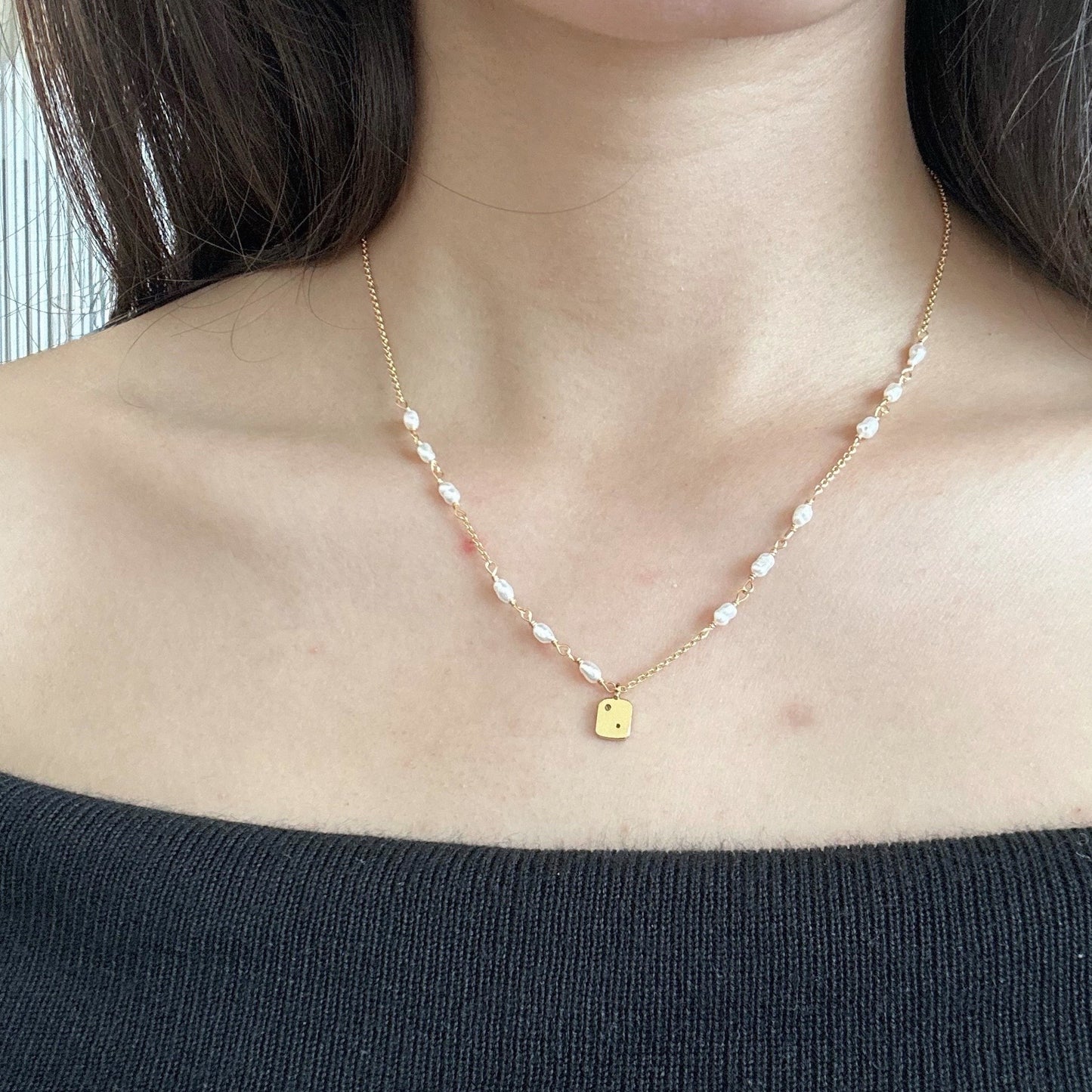 Gold necklace featuring a pearl and a gold charm, elegantly designed for a sophisticated look.