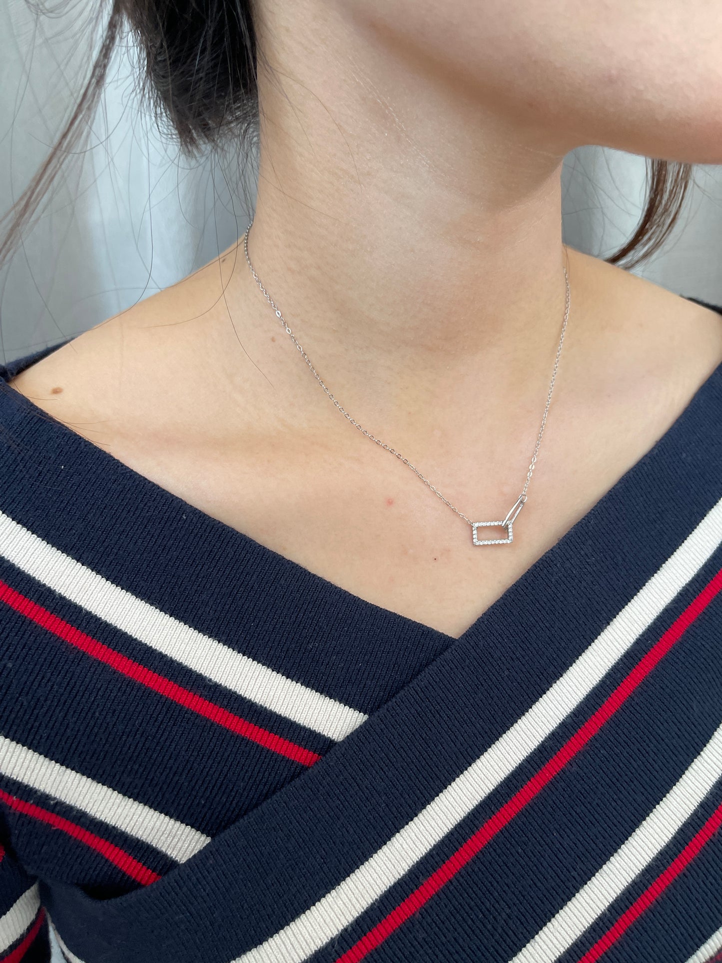 Delicate silver necklace with interlocking, diamond-encrusted rectangular shapes.