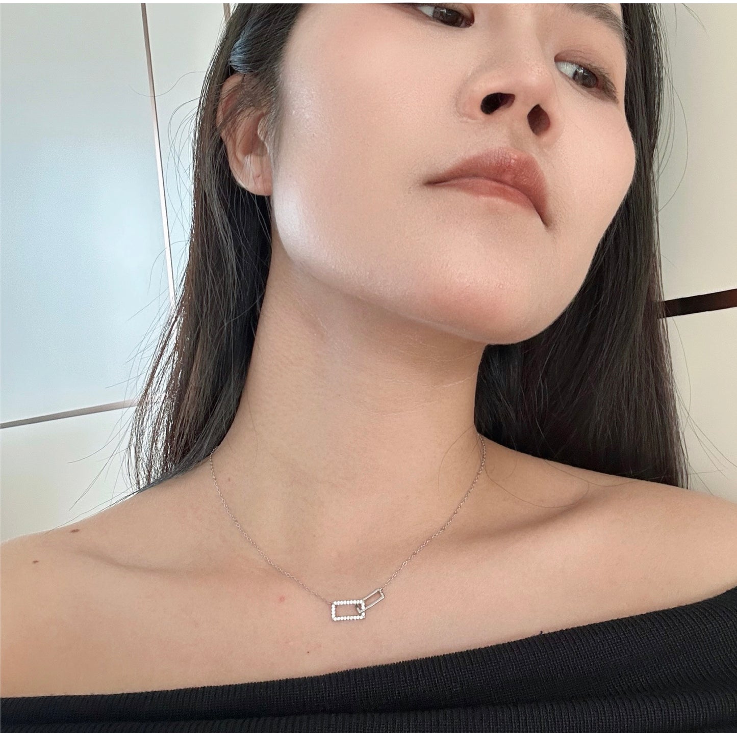 Close-up of a girl wearing a delicate silver necklace with interlocking, diamond-encrusted rectangular shapes.