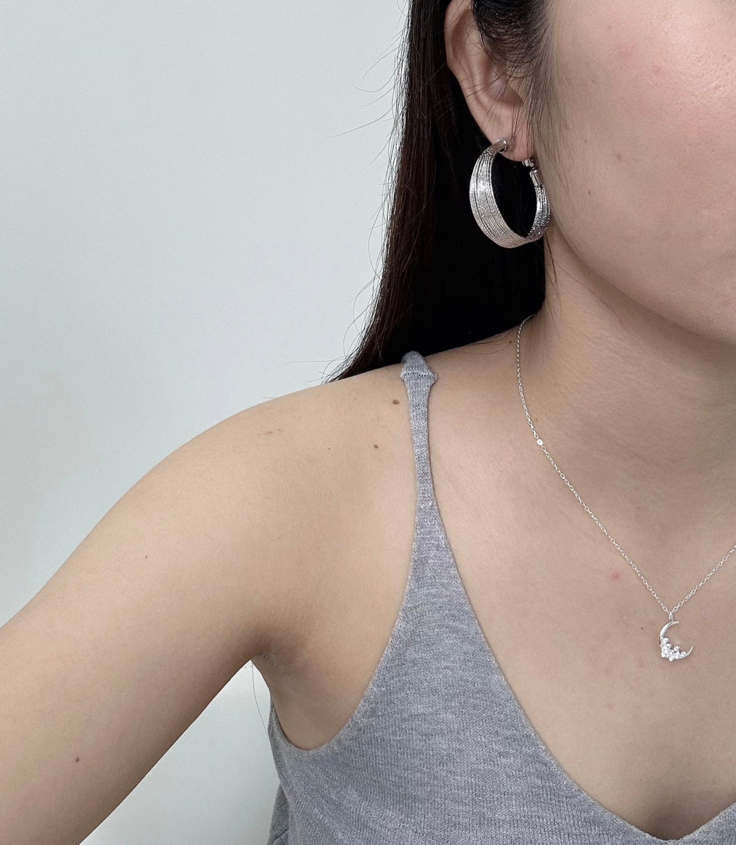 Close-up of a woman wearing a luxurious silver crescent necklace embellished with diamonds, presented on a simple, light-colored surface.