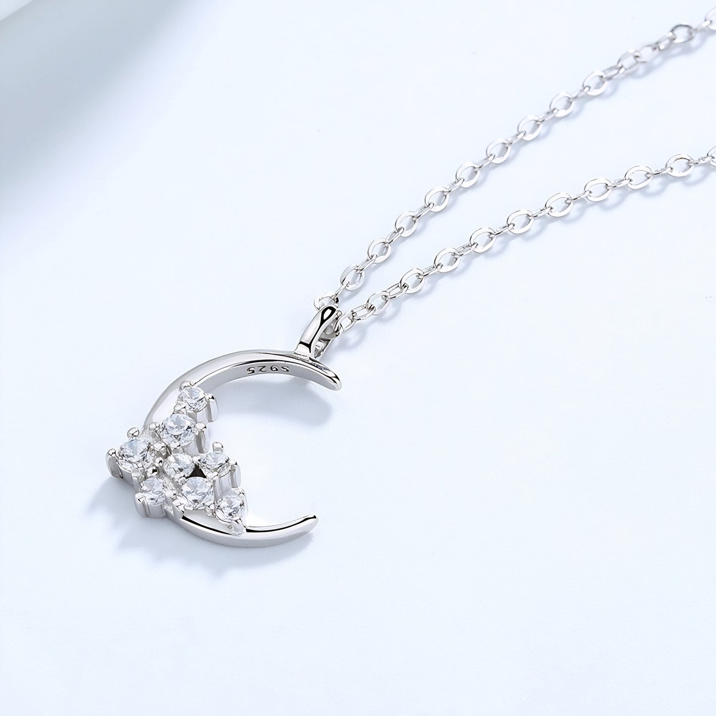 A luxurious silver crescent necklace embellished with diamonds, presented on a simple, light-colored surface.