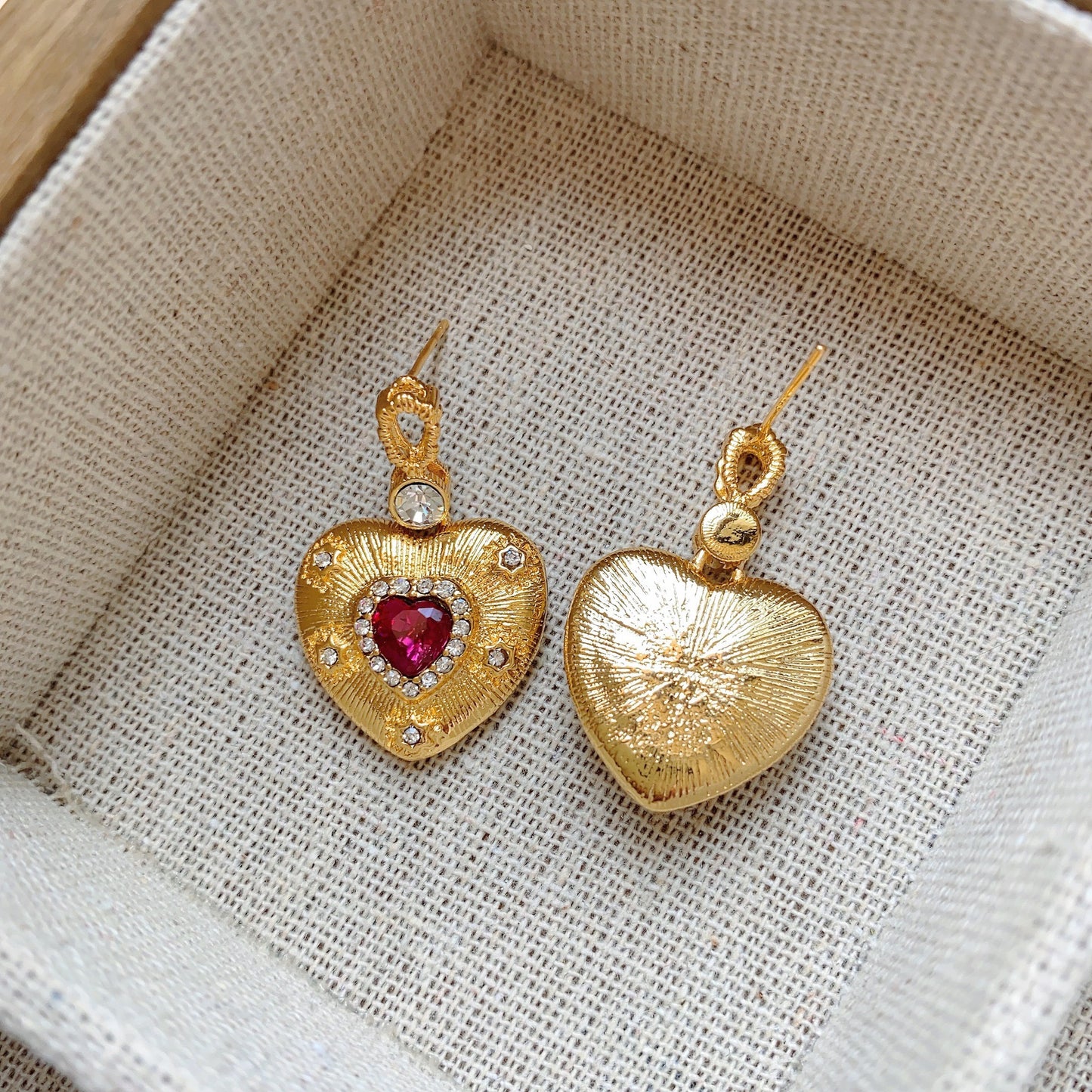 Gold heart-shaped earrings with ruby-red centers and small white crystals.