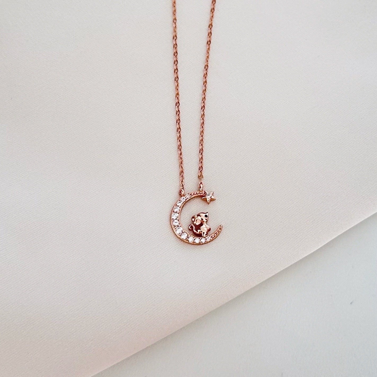 Rose gold necklace with a crescent moon charm, featuring a small cat and crystals, and a star.