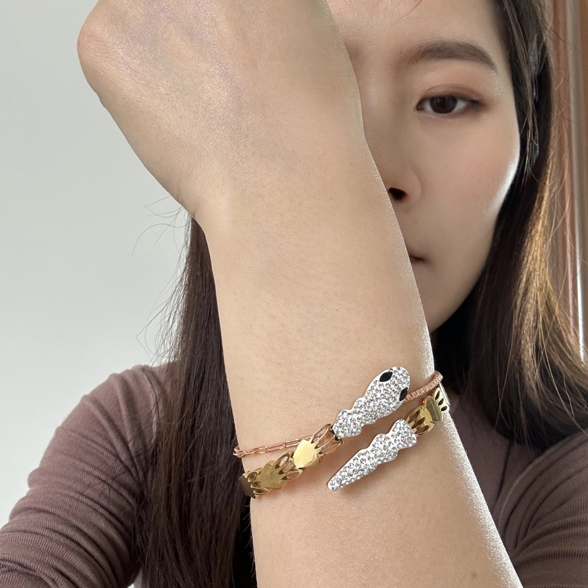 Close-up of a woman wearing gold bangle bracelet with a snake design, featuring clear and black crystals.