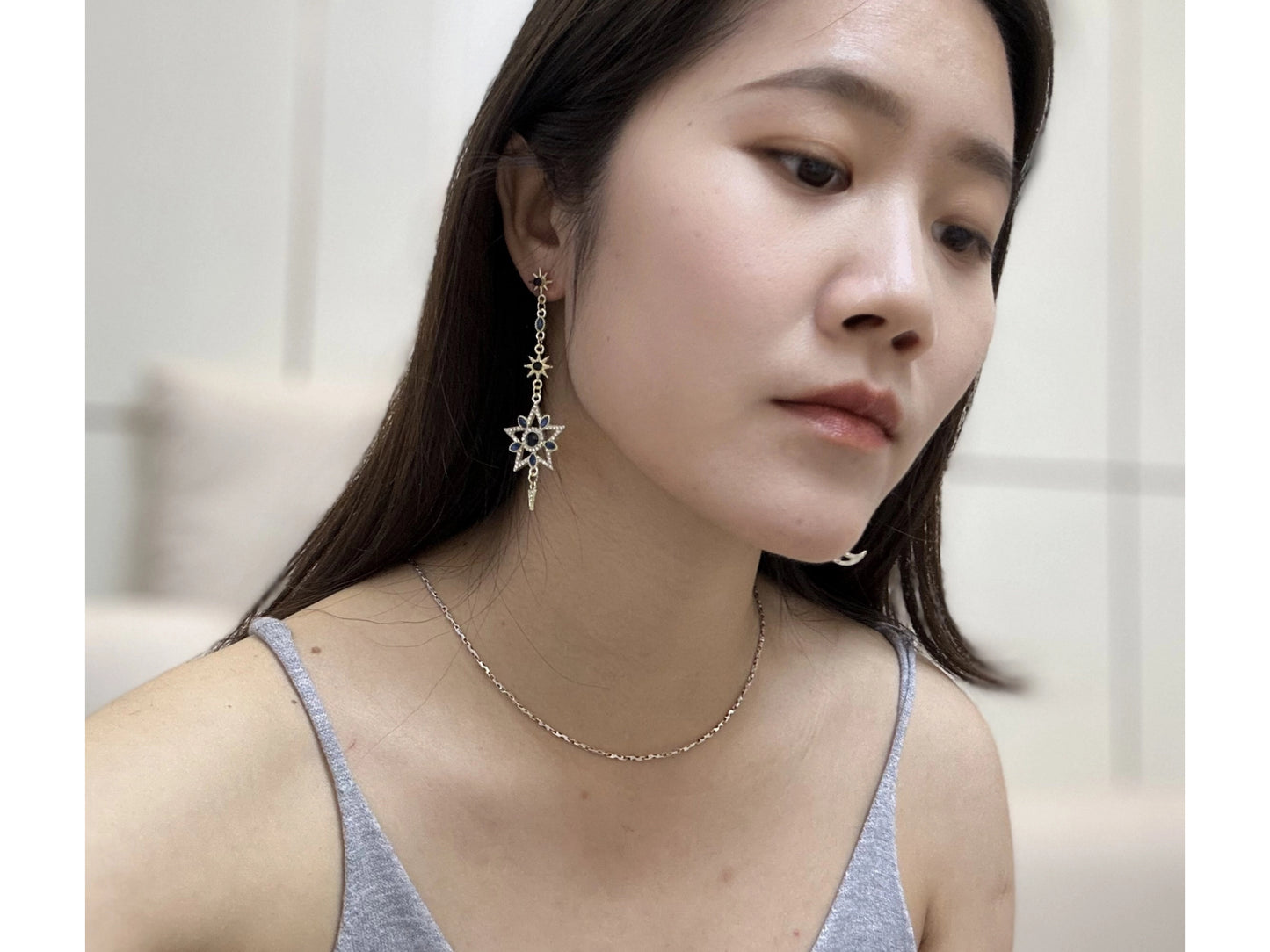 Close up of a woman wearing gold-tone earrings featuring detailed moon, star, and sun designs adorned with white crystals and dark blue gemstones.