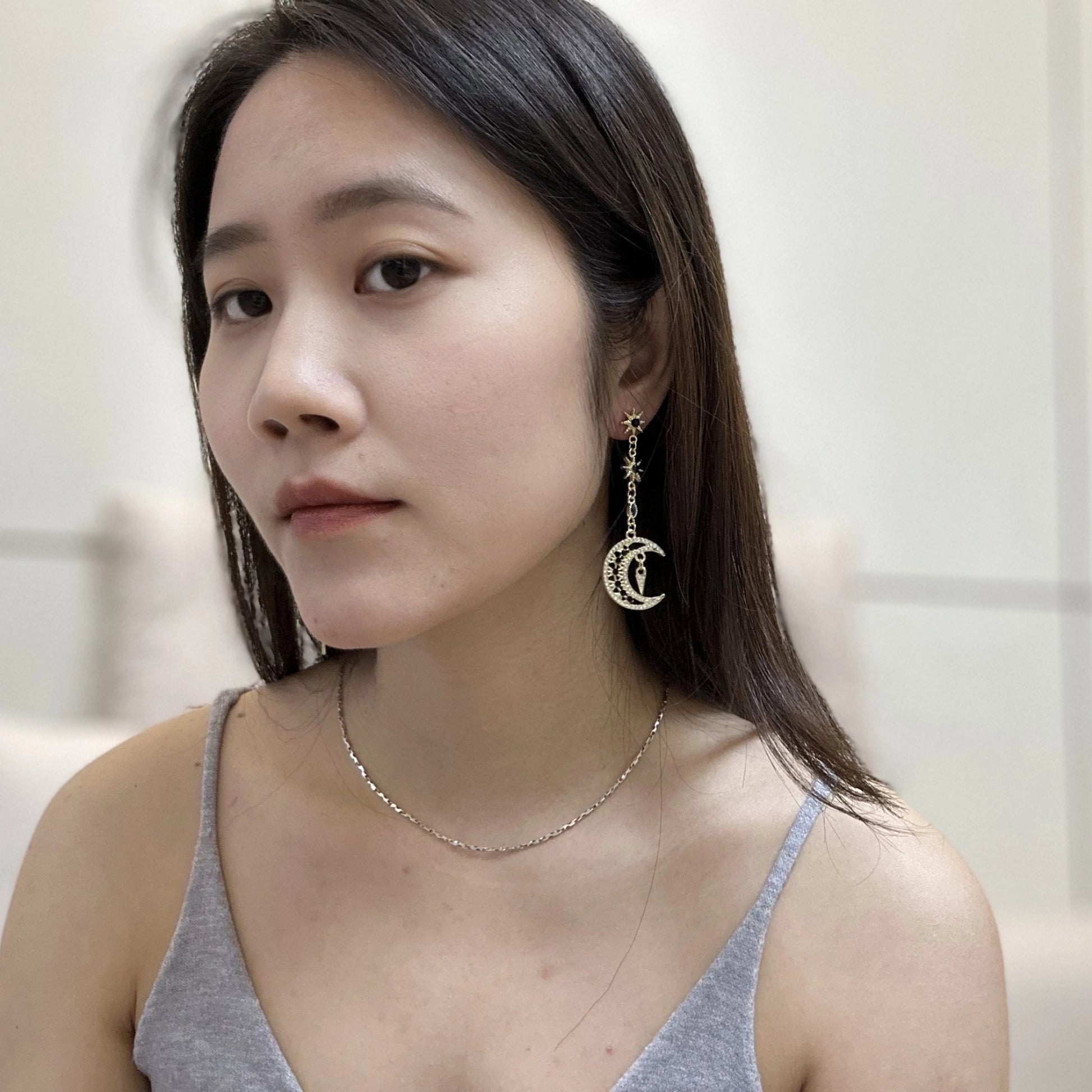 Close up of a woman wearing Gold-tone earrings featuring detailed moon, star, and sun designs adorned with white crystals and dark blue gemstones.
