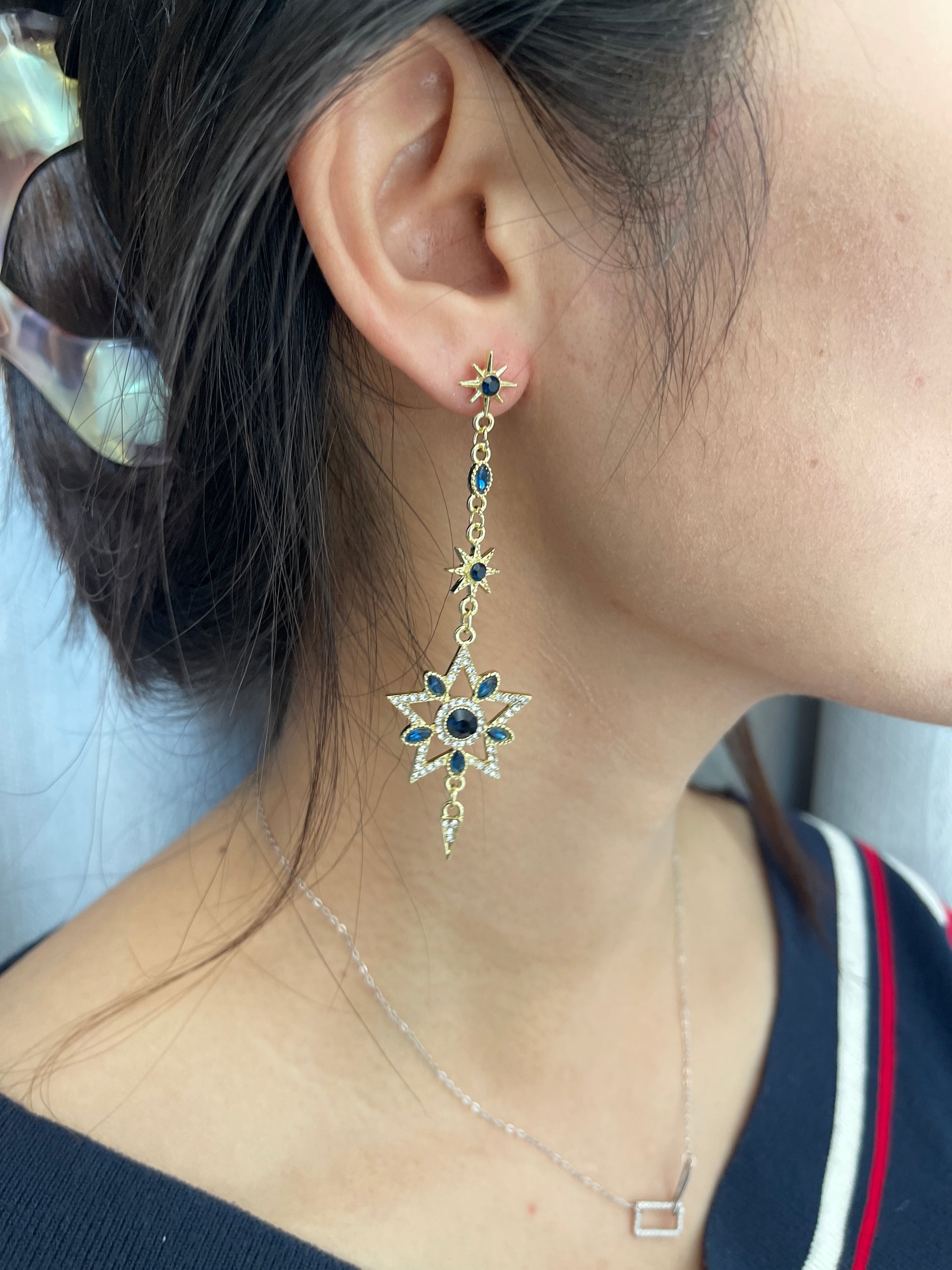 Gold-tone earrings featuring detailed moon, star, and sun designs adorned with white crystals and dark blue gemstones.