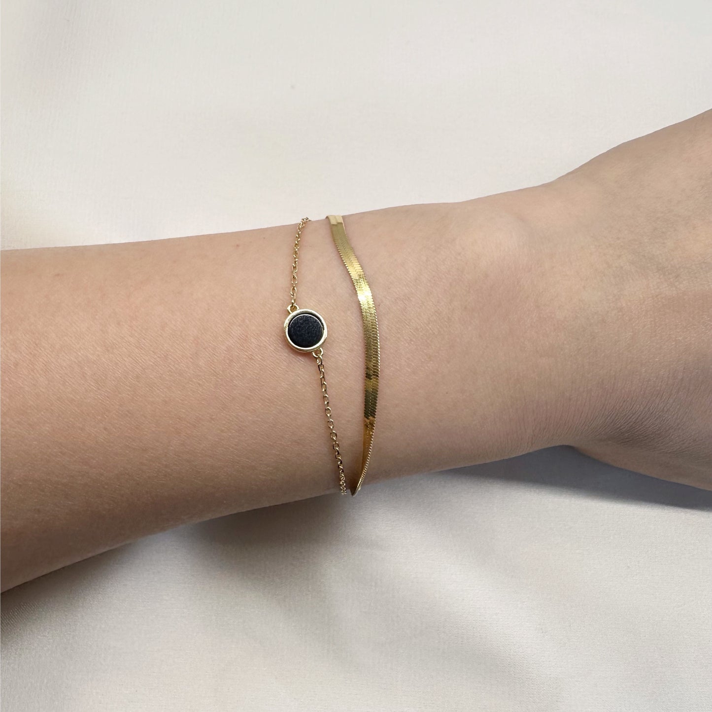 Close-up of a wrist wearing a gold bracelet with a black circle charm.