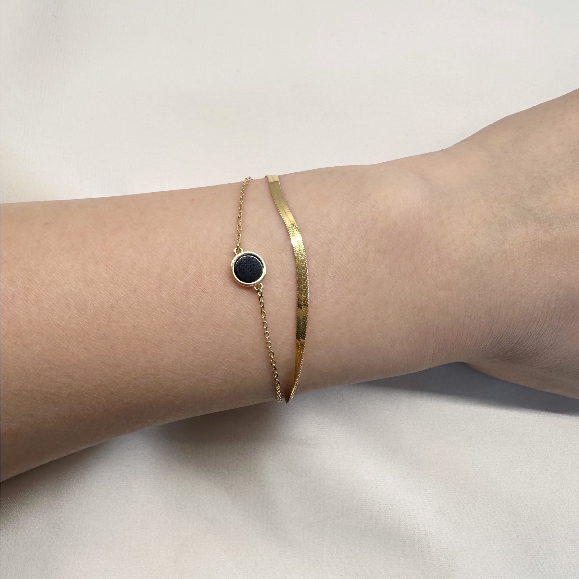 Close-up of a wrist wearing a gold bracelet with a black circle charm.