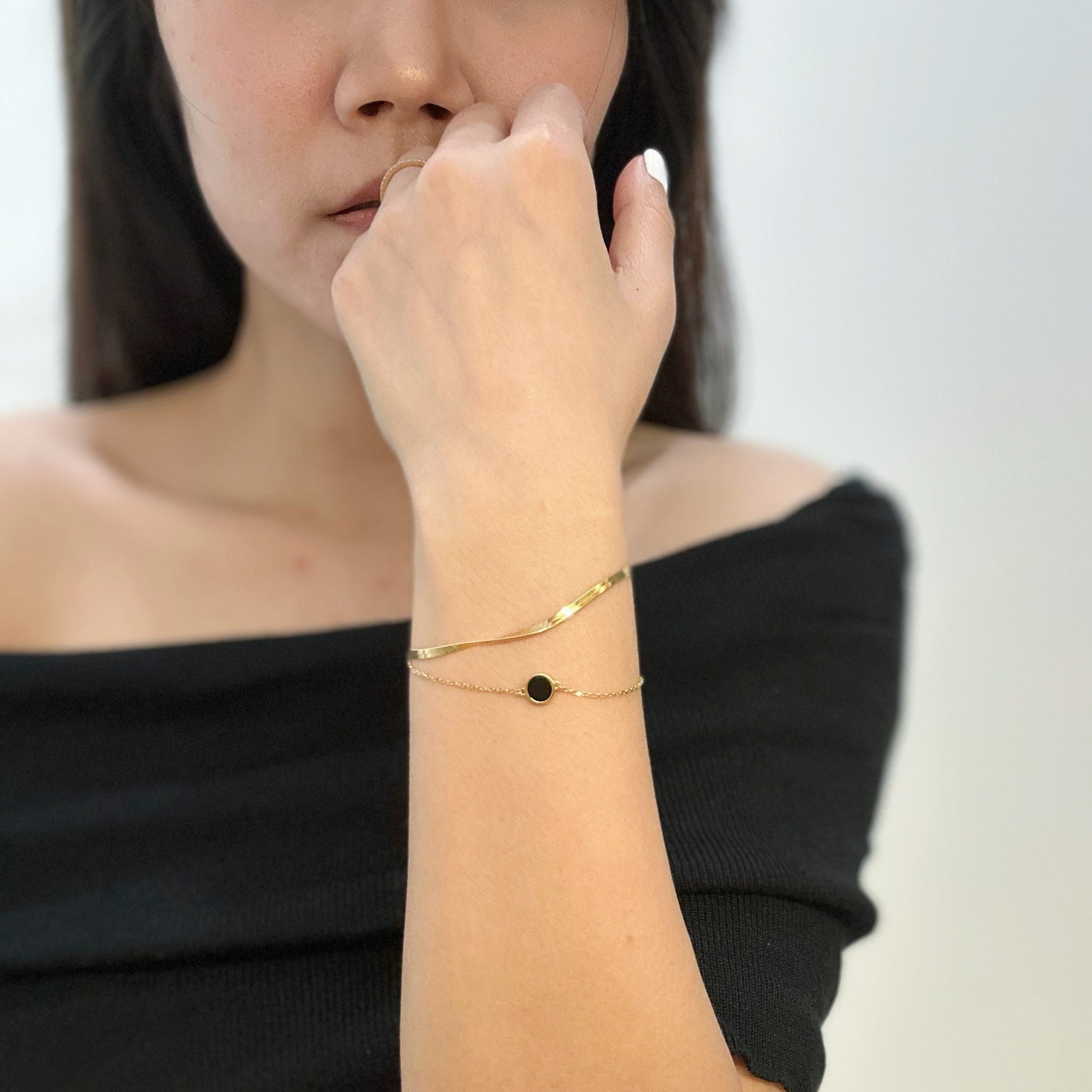 Close-up of a woman wearing a gold bracelet with a black circle charm and pearl earrings.