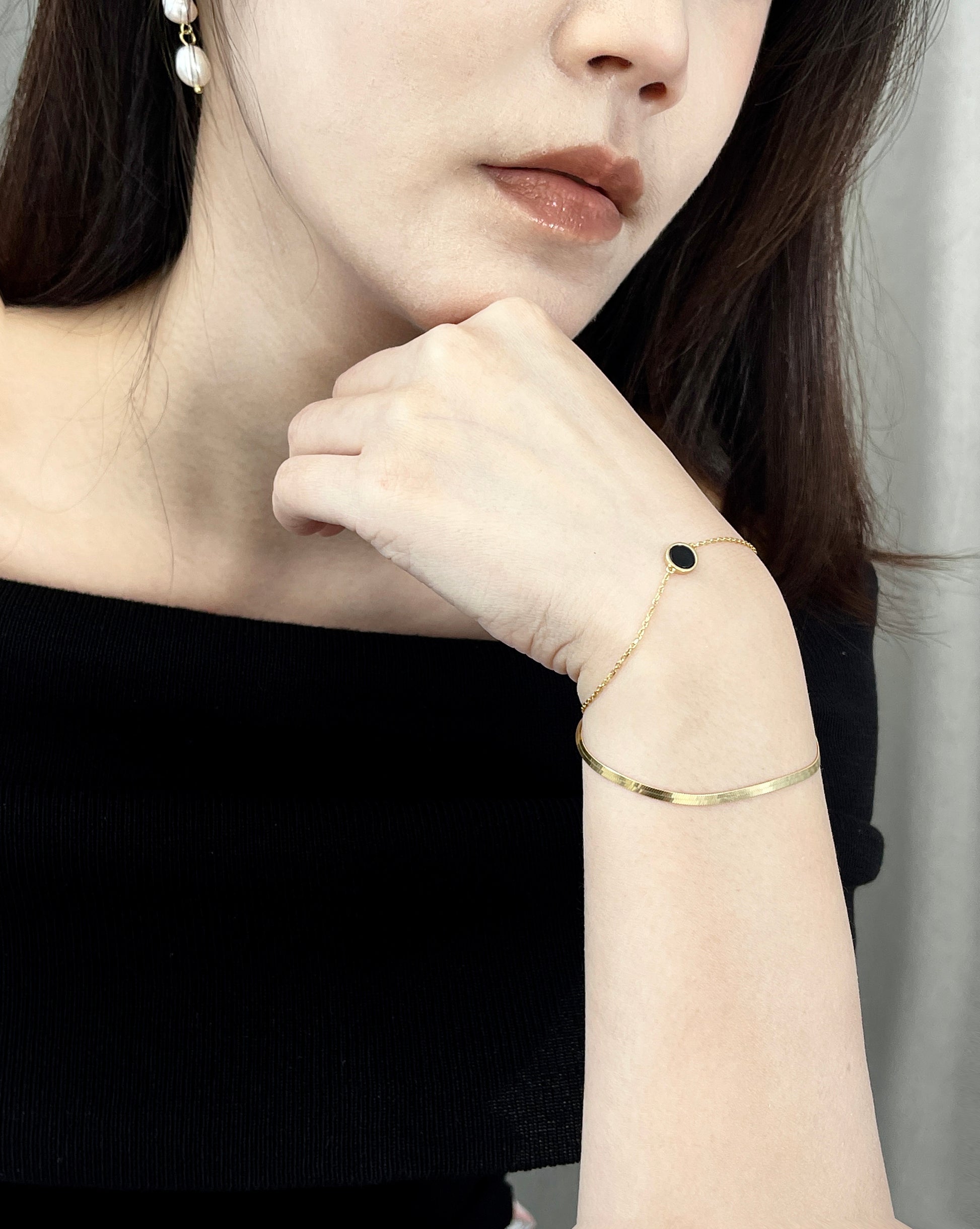 Close-up of a woman wearing a gold bracelet with a black circle charm and pearl earrings.