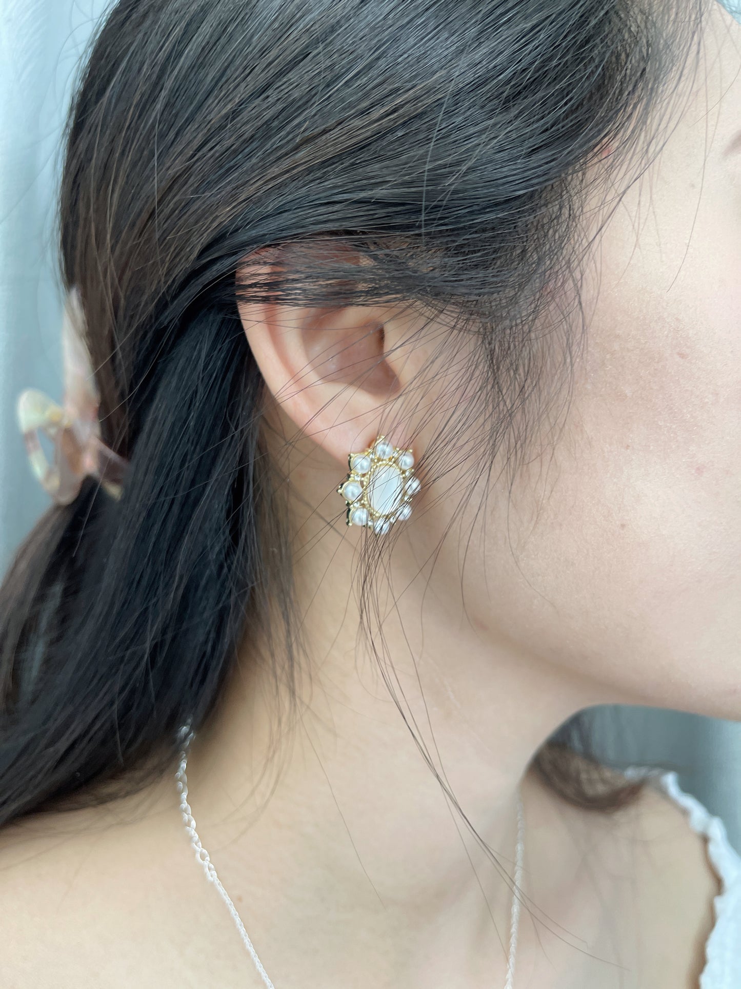 Close-up of a woman wearing gold stud earrings decorated with small white pearls, and a delicate necklace.