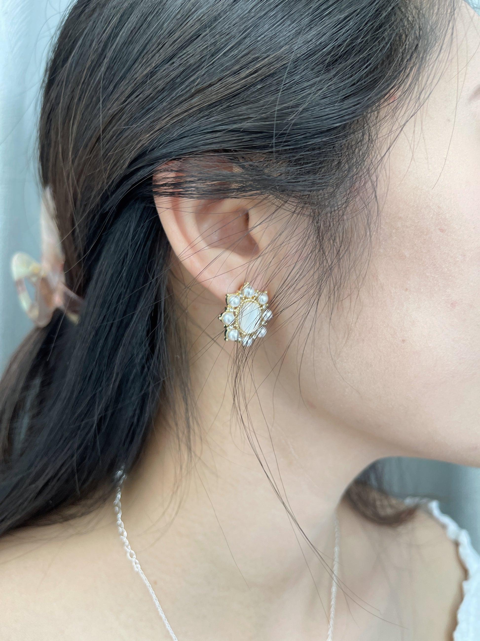 Close-up of a woman wearing gold stud earrings decorated with small white pearls, and a delicate necklace.