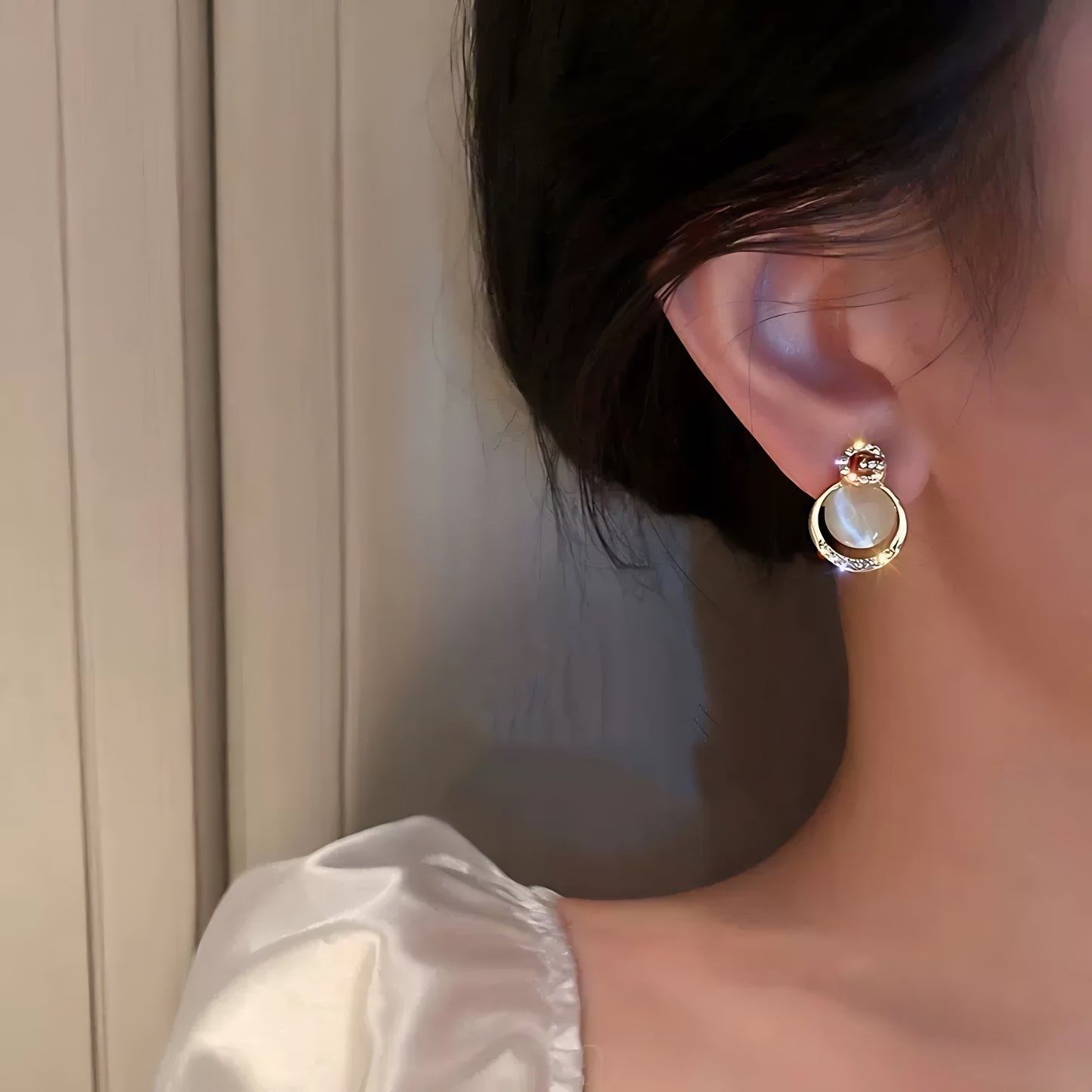 close-up of a woman wearing gold hoop earrings with white opal-like stones and the letter "G" outlined in crystals.