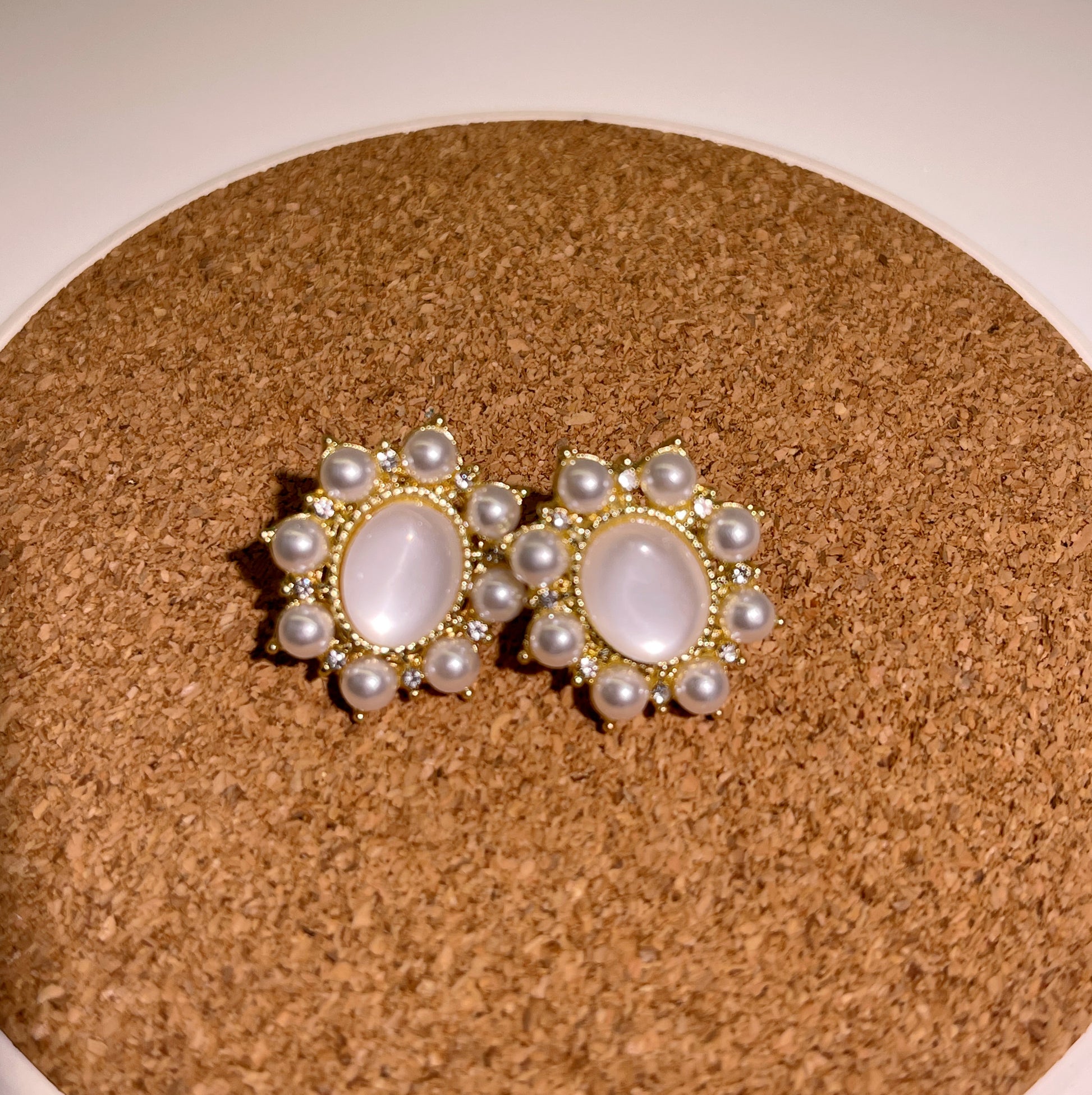Pair of gold-tone stud earrings featuring a centered, oval mother-of-pearl stone, surrounded by a cluster of small pearls and tiny diamonds.