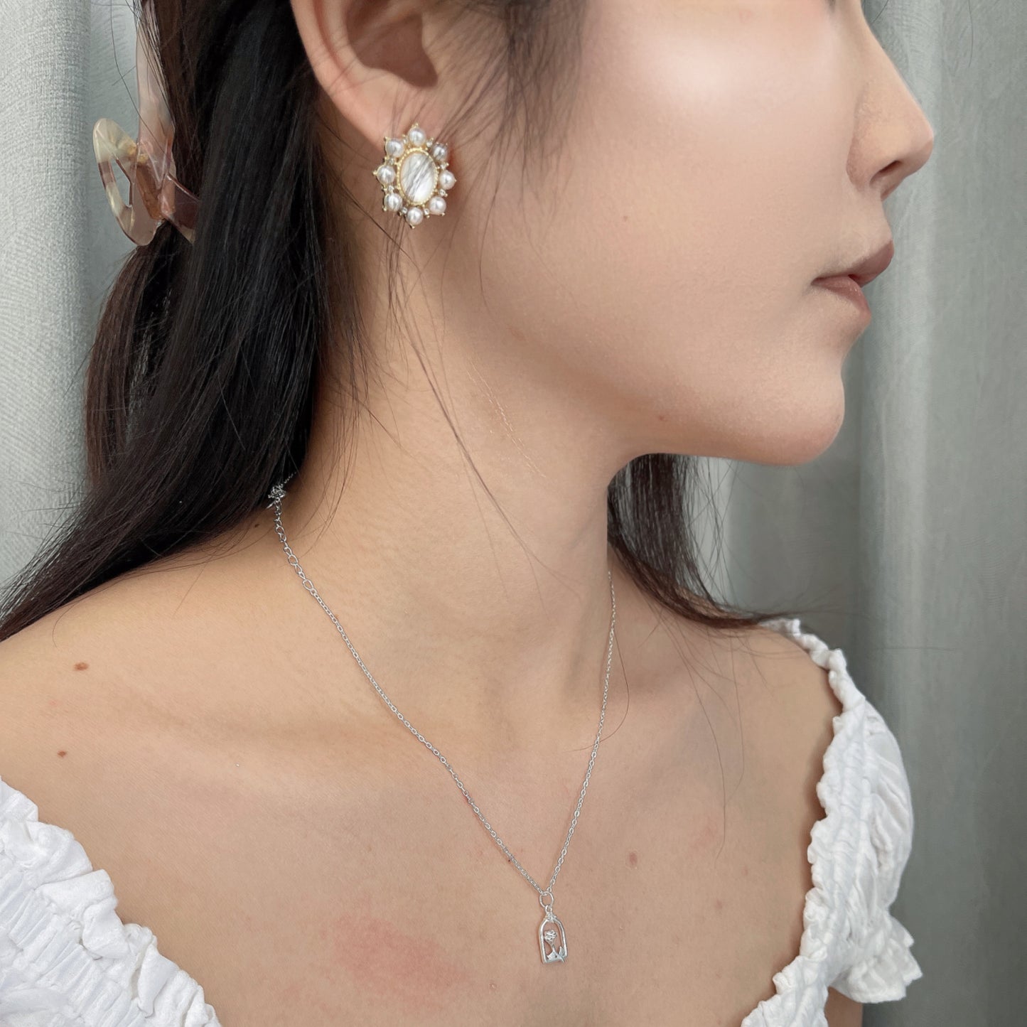 Close-up of a woman wearing gold stud earrings decorated with small white pearls, and a delicate necklace.