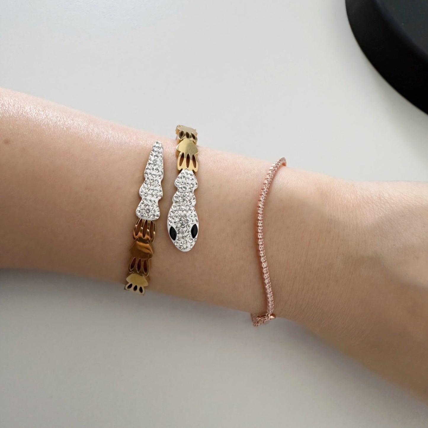 Gold bangle bracelet with a snake design, featuring clear and black crystals.