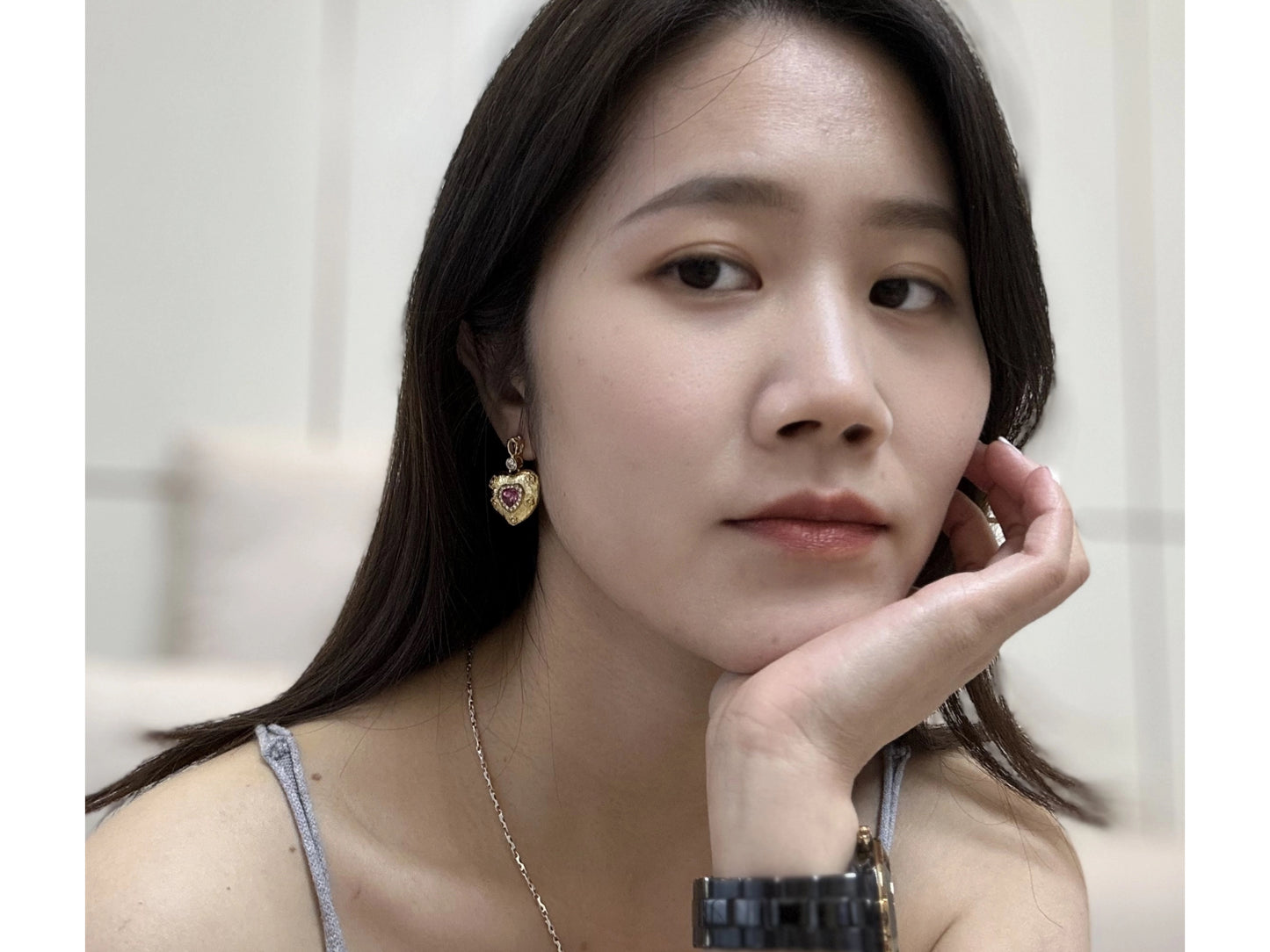 Close up of a woman wearing a pair of gold heart-shaped earrings with ruby-red centers and small white crystals.