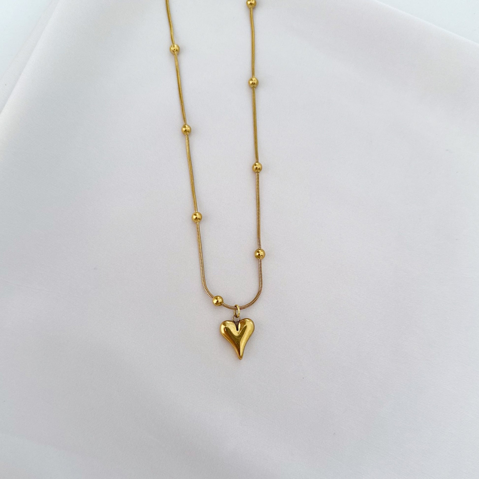 Gold necklace with a heart-shaped pendant and small ball accents.