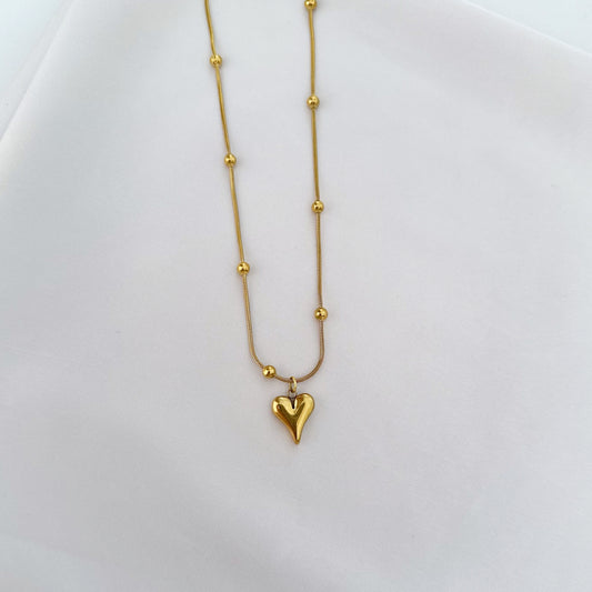 Gold necklace with a heart-shaped pendant and small ball accents.