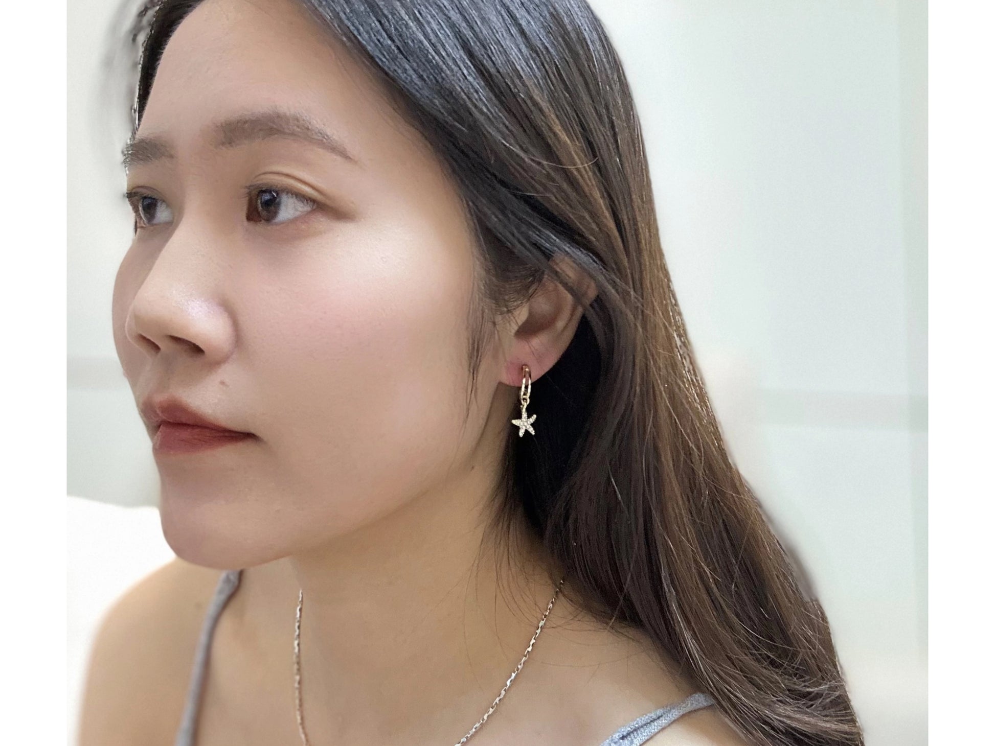 Close up of a woman wearing a pair of gold tone elegant starfish drop earrings