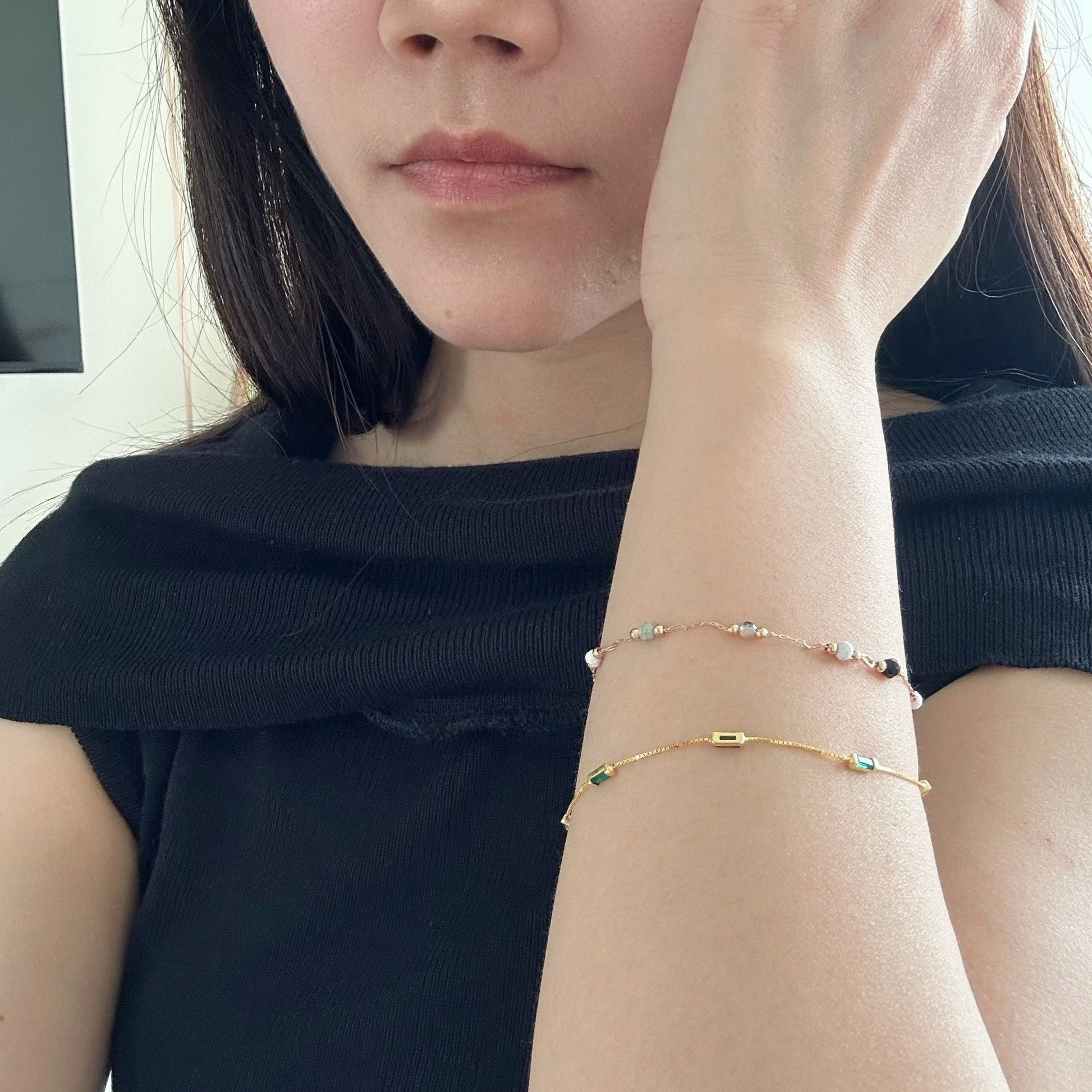 Woman wearing a gold bracelet with small, emerald-green stones and small beads.