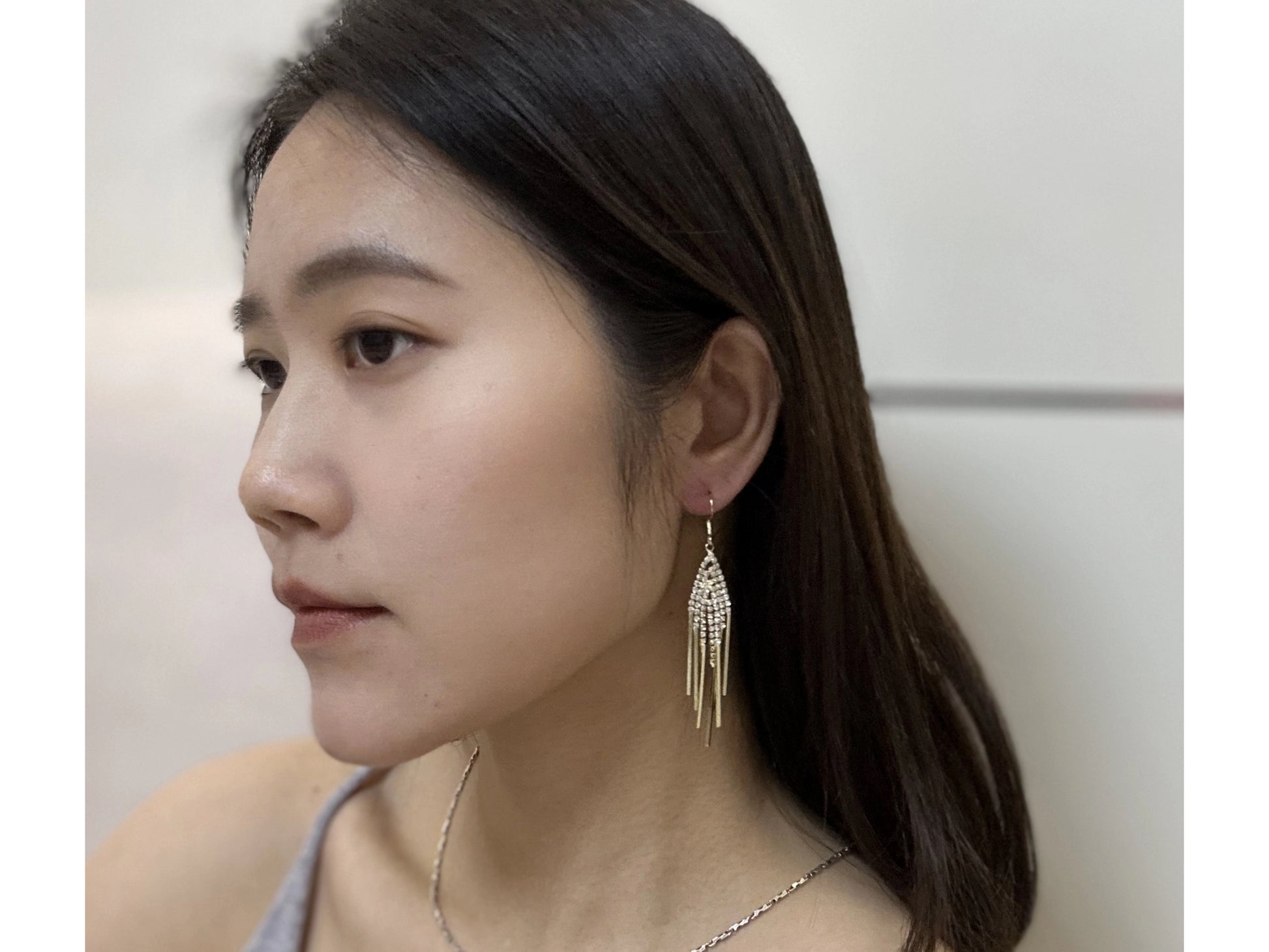 Close-up of a woman wearing gold-tone dangle earrings with teardrop-shaped, crystal-encrusted, cascading accents.

