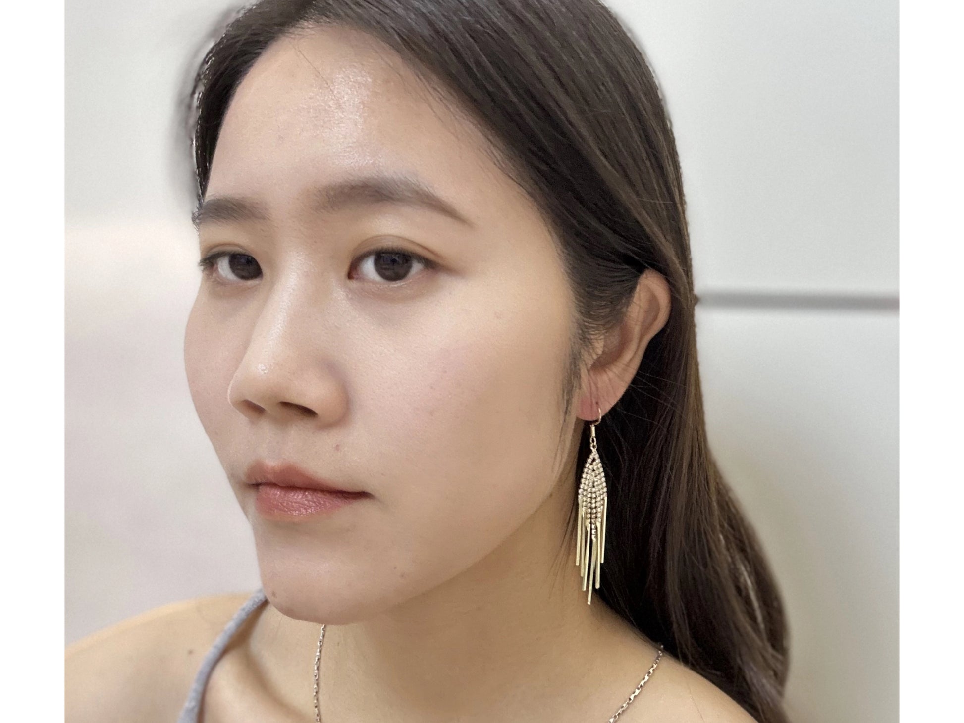Close up of a woman wearing gold-tone dangle earrings with teardrop-shaped, crystal-encrusted, cascading accents.

