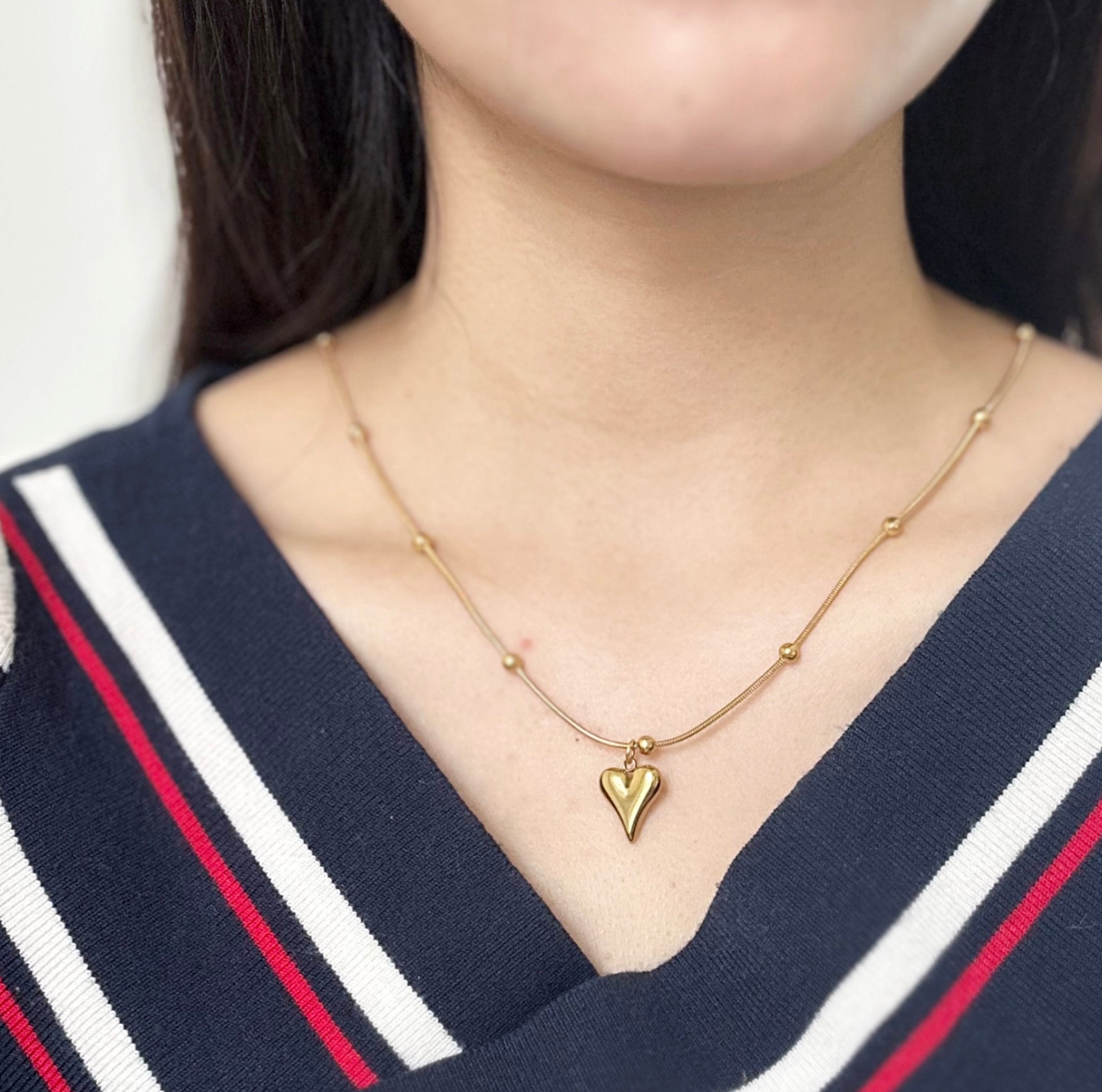 Close up of a woman wearing gold necklace with a heart-shaped pendant and small ball accents.