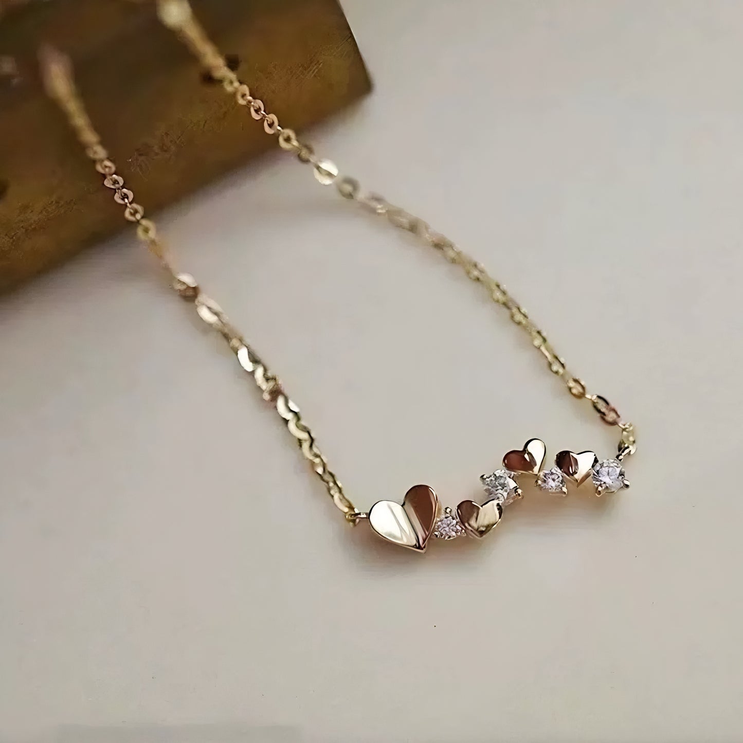 Gold necklace with small heart-shaped pendants and clear stones.