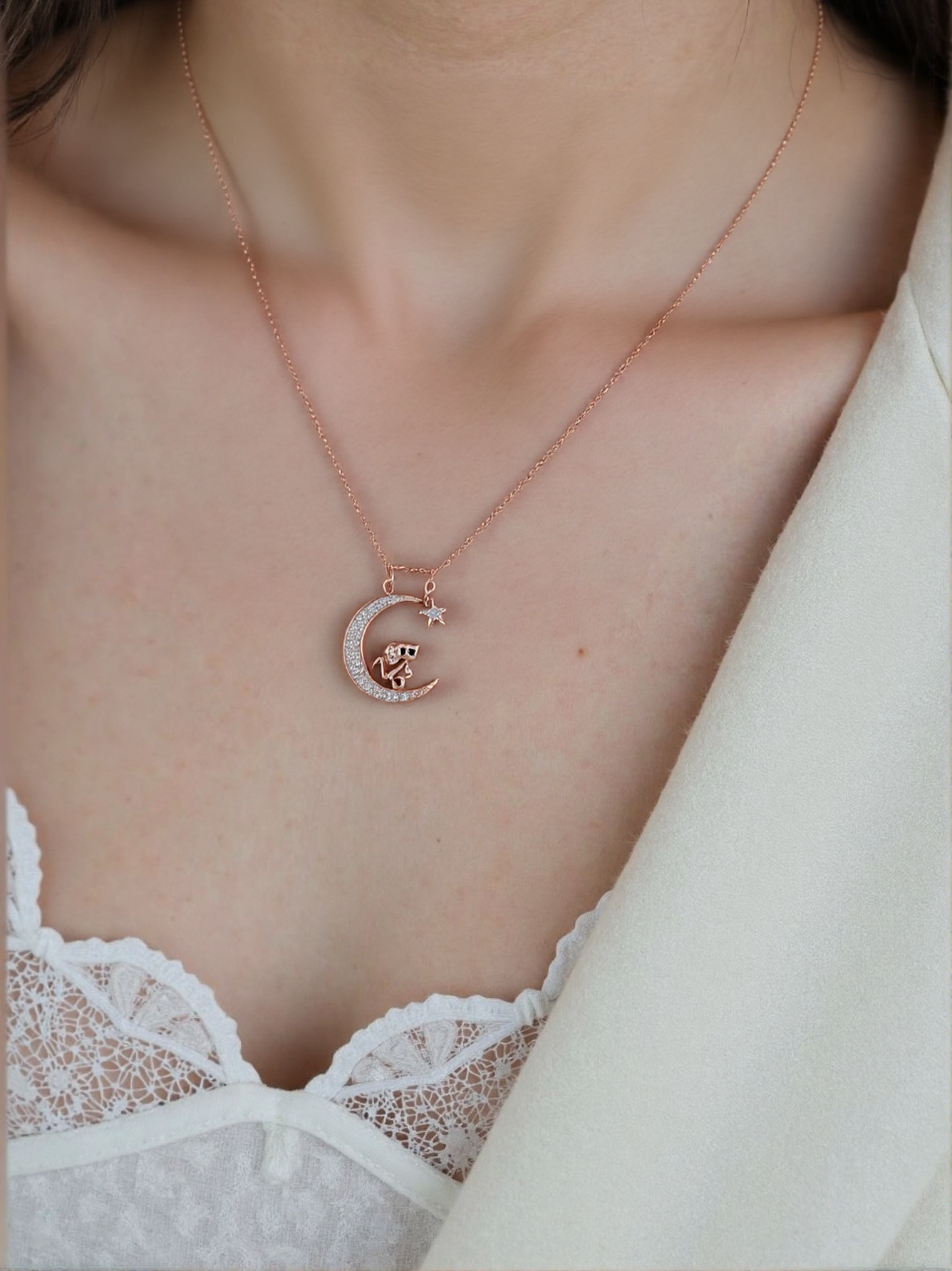 Close-up of a woman wearing a rose gold necklace, with a moon charm, featuring a small mouse and crystals, and a star.