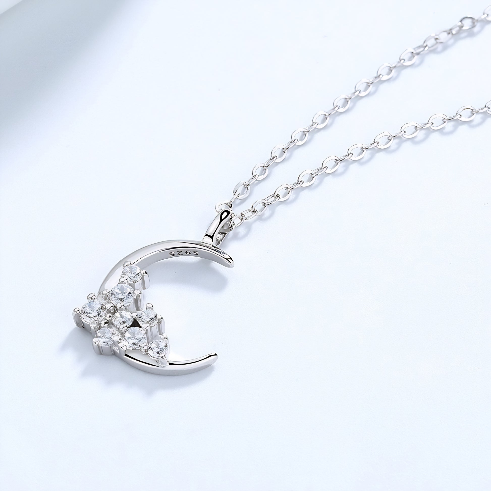 A luxurious silver crescent necklace embellished with diamonds, presented on a simple, light-colored surface.