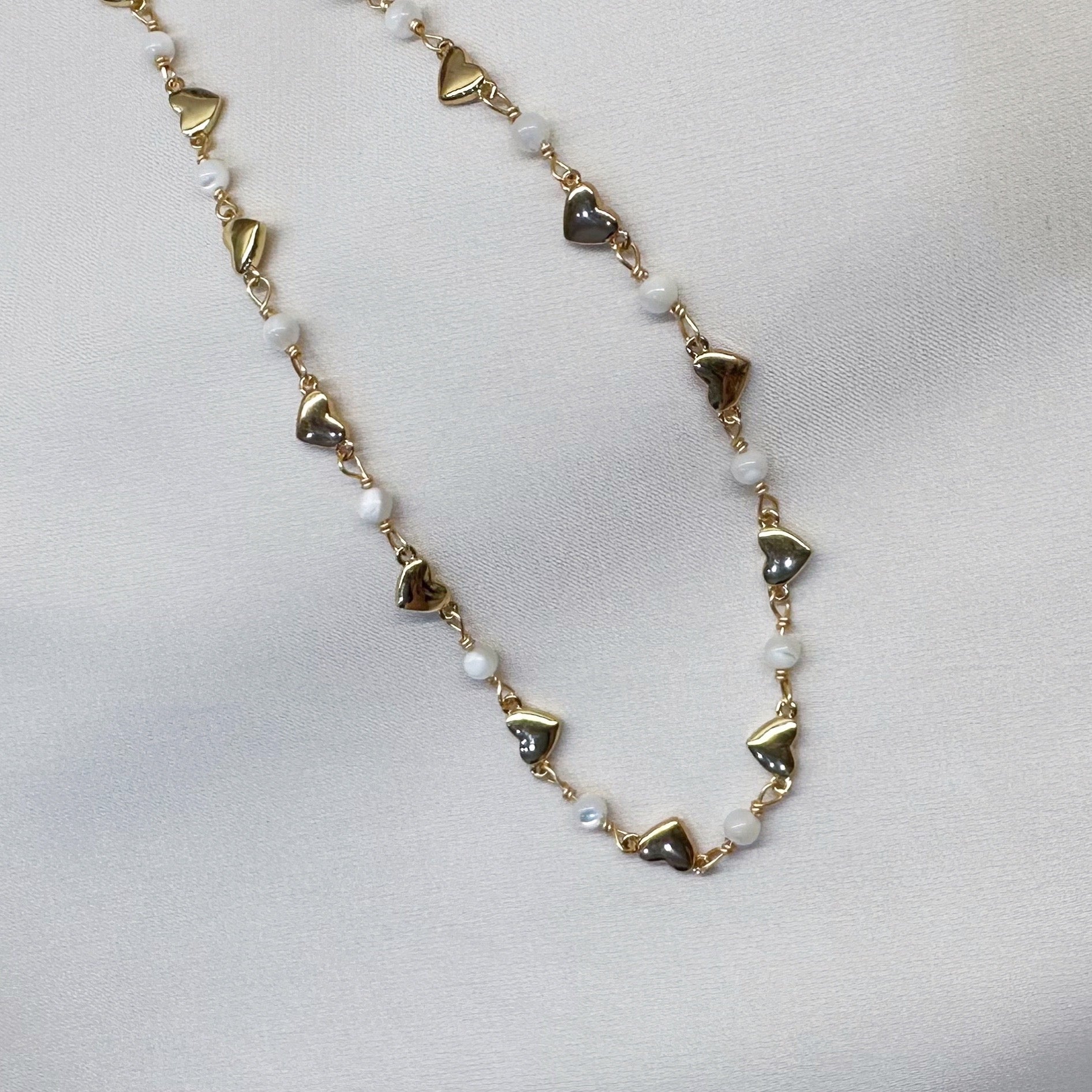 Gold chain adorned with small heart-shaped charms, elegantly showcasing a delicate and romantic design.