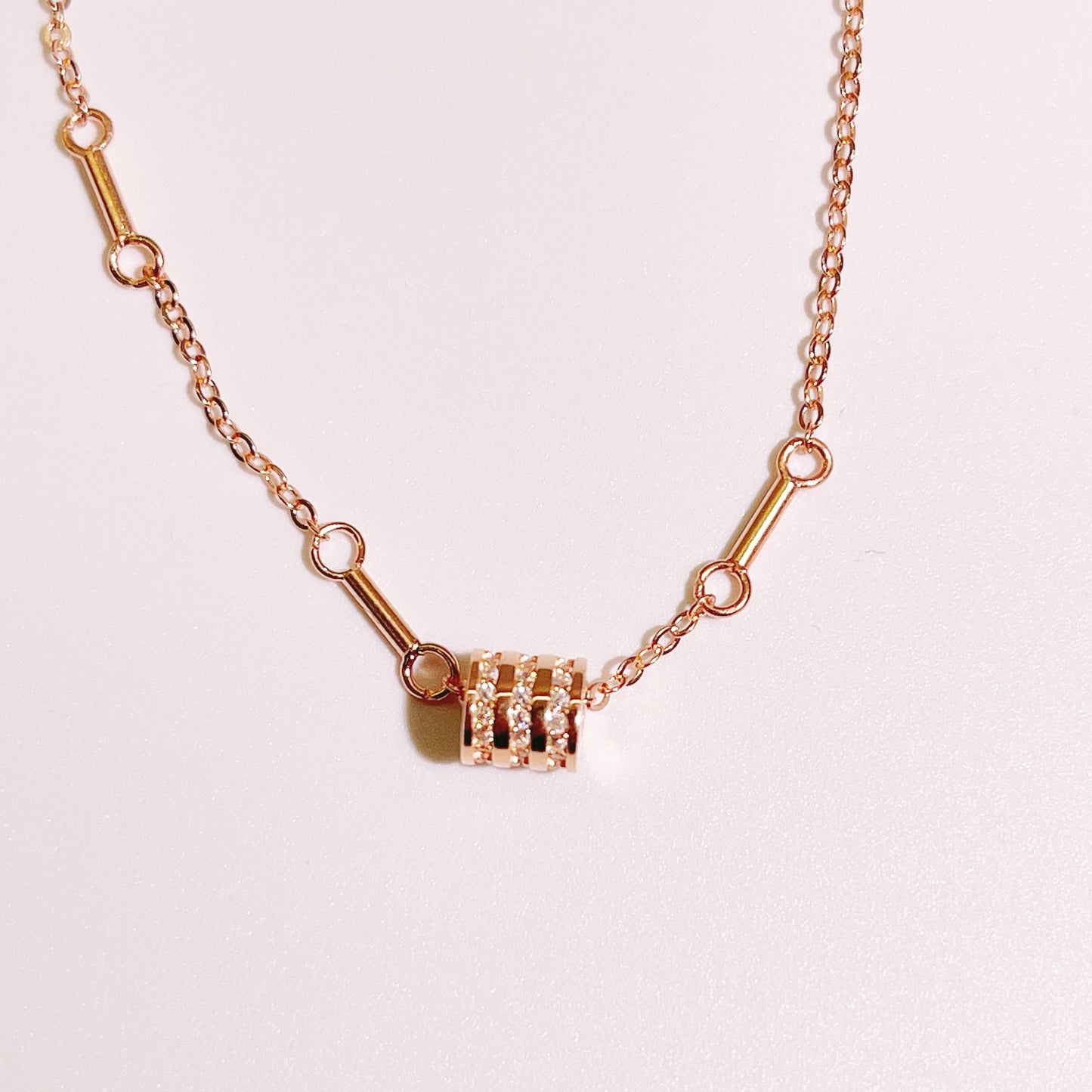 Rose gold bracelet with a cylindrical pendant encrusted with small diamonds.
