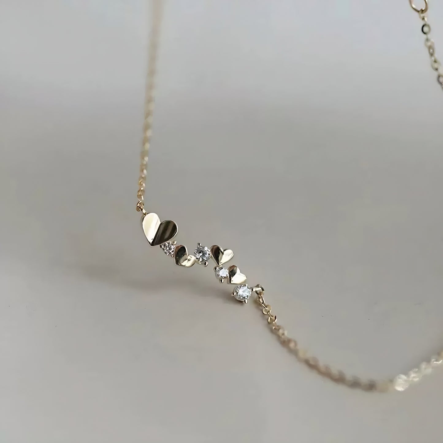 Gold necklace with small heart-shaped pendants and clear stones.