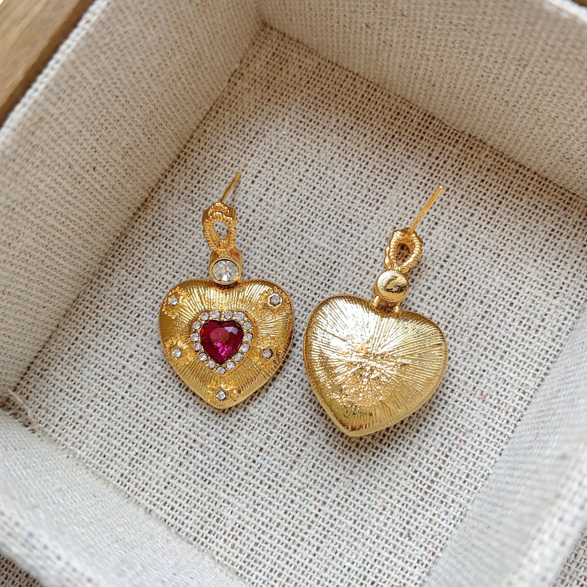 Gold heart-shaped earrings with ruby-red centers and small white crystals.