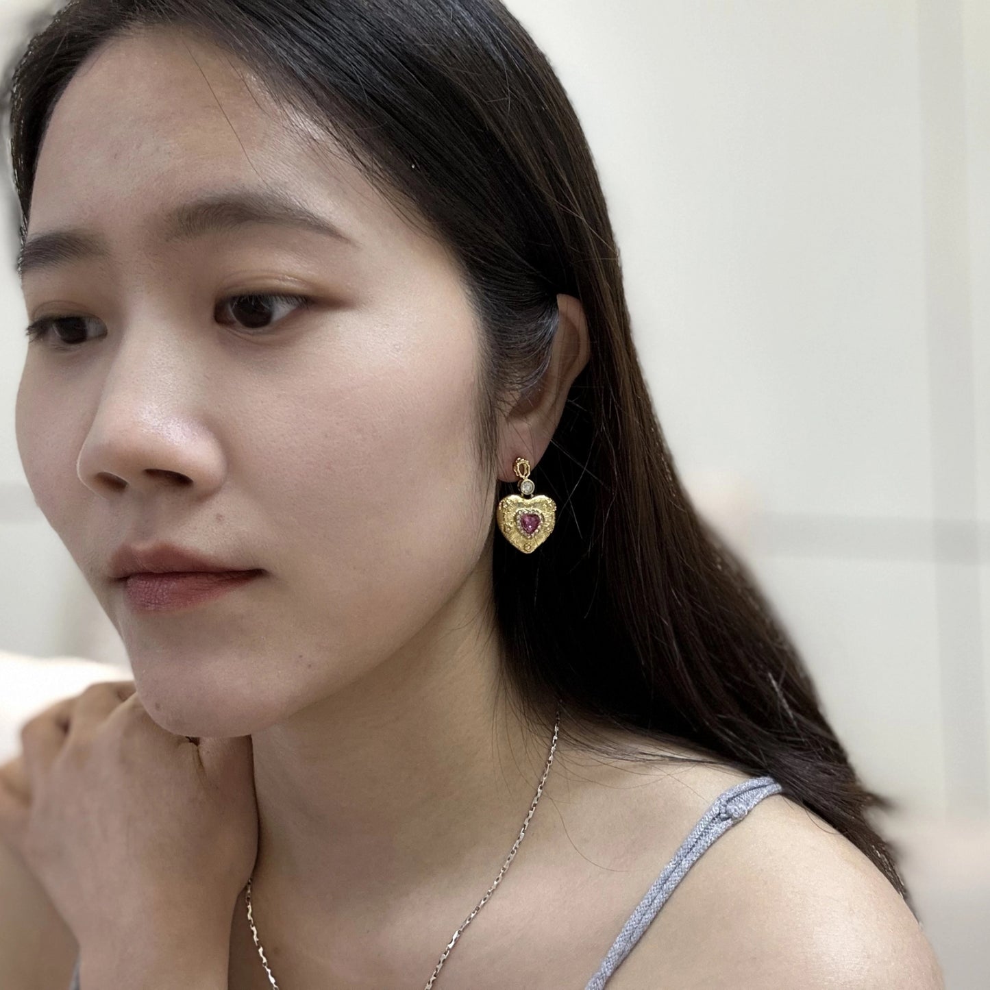 Close up of a woman wearing gold heart-shaped earrings with ruby-red centers and small white crystals.