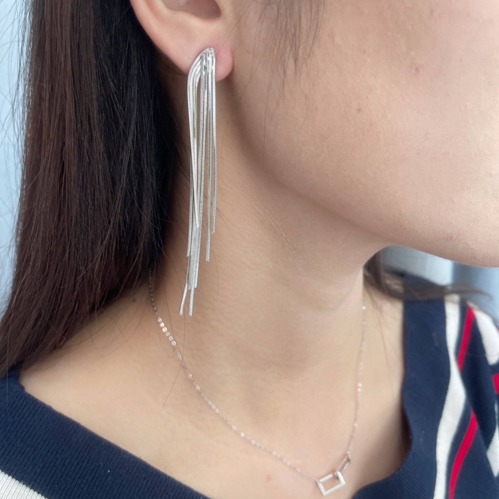 Close-up of a woman wearing a pair of silver-tone, cascading, textured chain dangle earrings.