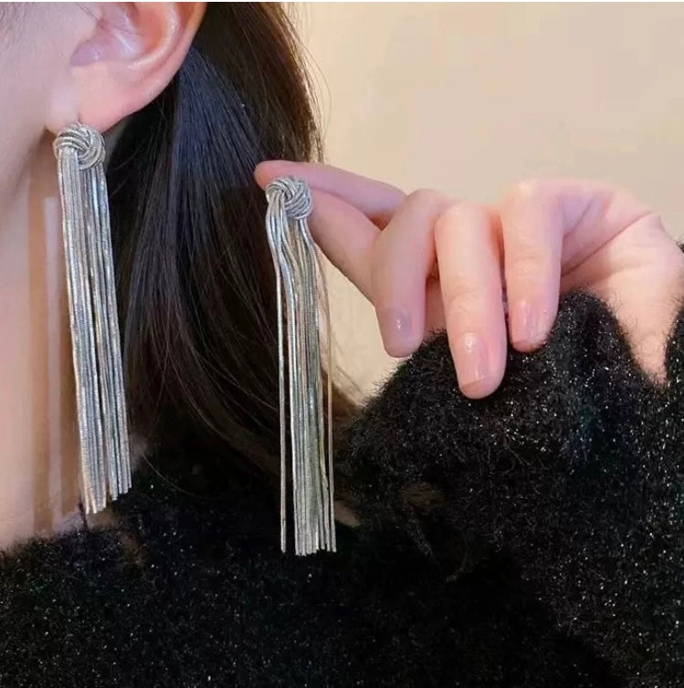 Close-up of a woman wearing silver-toned, layered tassel earrings with knotted tops.
