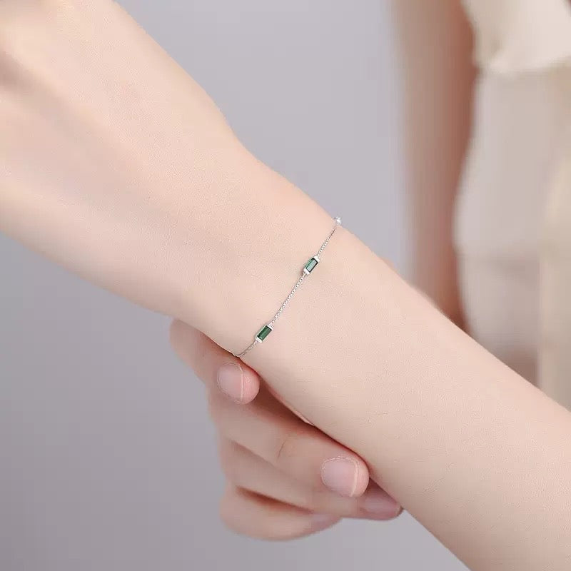 Close-up of a wrist wearing delicate silver bracelet with emerald-cut green stones.