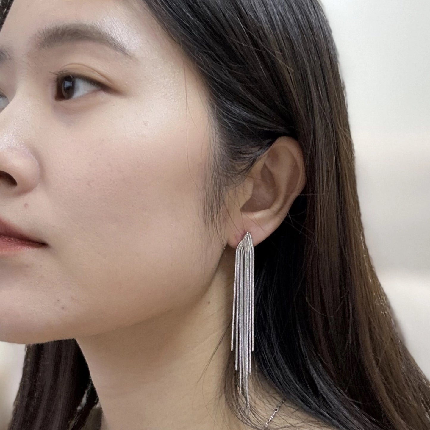 Close-up of a woman wearing a pair of silver-tone, cascading, textured chain dangle earrings.
