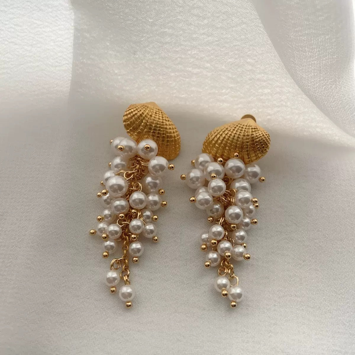 Gold-tone seashell earrings with cascading pearl accents.