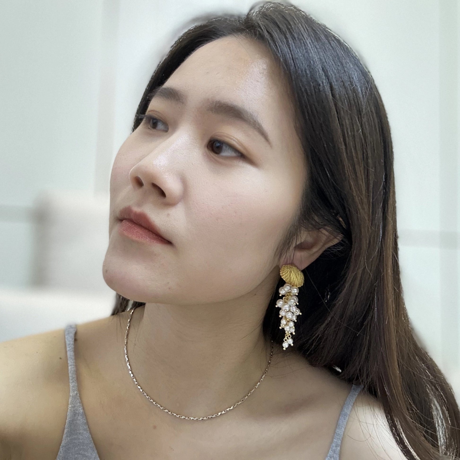 Close-up of a woman wearing gold-tone seashell earrings with cascading pearl accents.