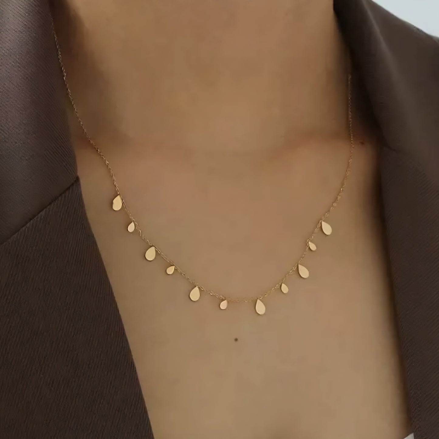 Close up of a women wearing a gold necklace with water drop and disc-shaped charms.