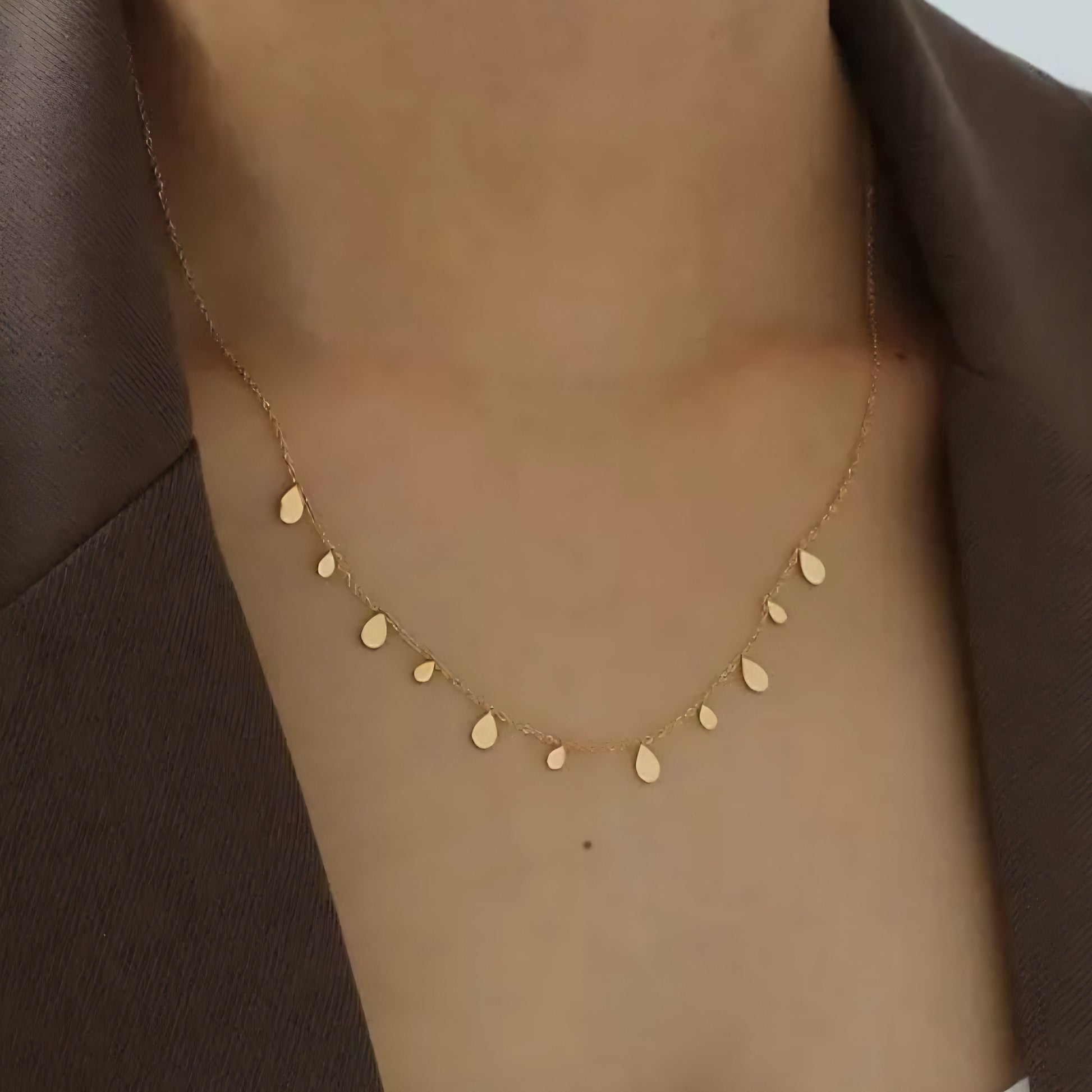 Close up of a women wearing a gold necklace with water drop and disc-shaped charms.